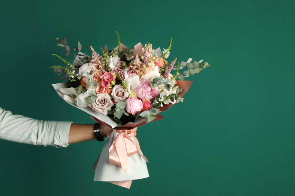 Mann hält einen schönen Blumenstrauß vor grünem Hintergrund, Nahaufnahme. Platz für Text.